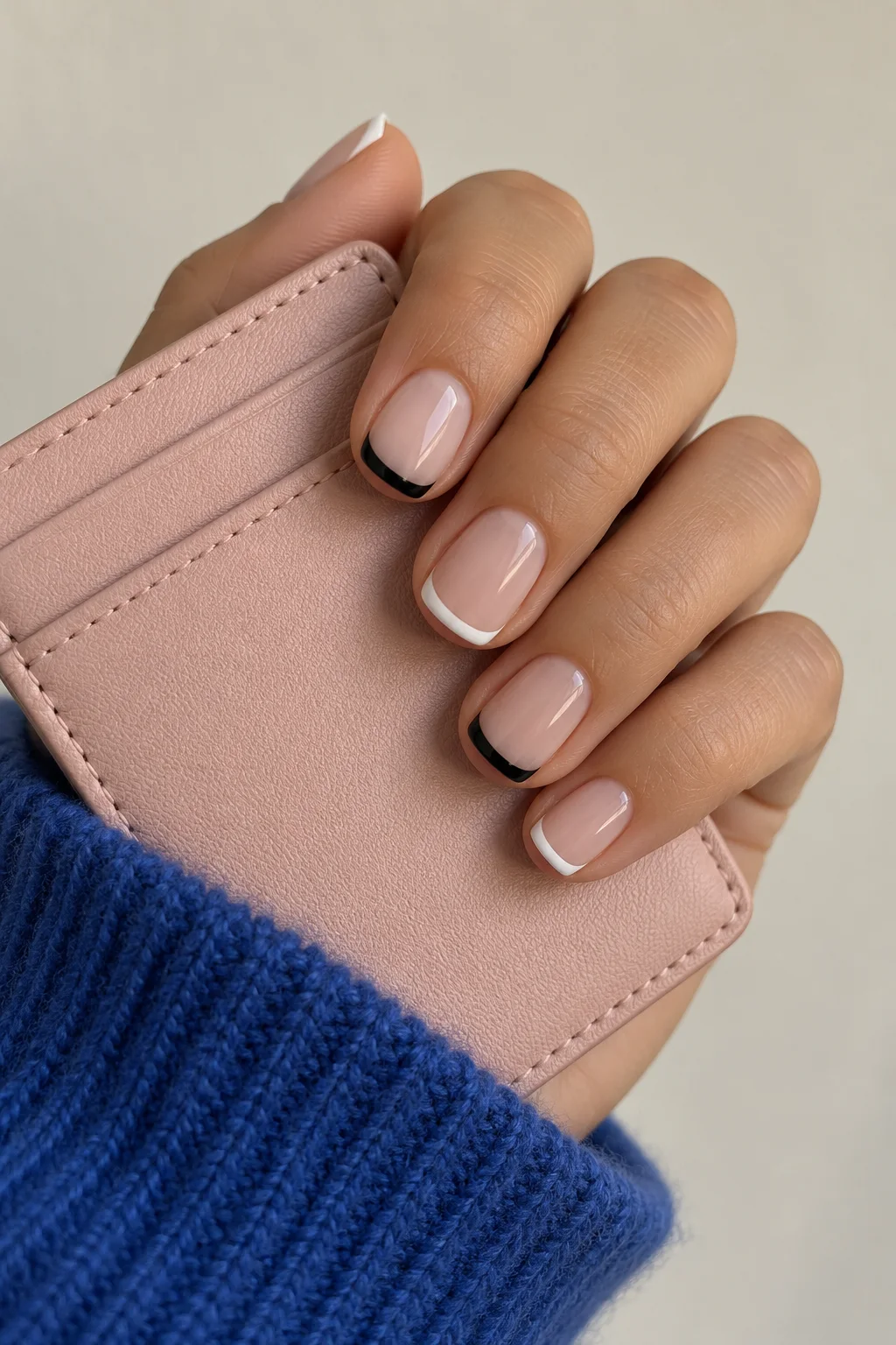 Alternating black and white French tips holding a blush cardholder with a cobalt knit cuff.