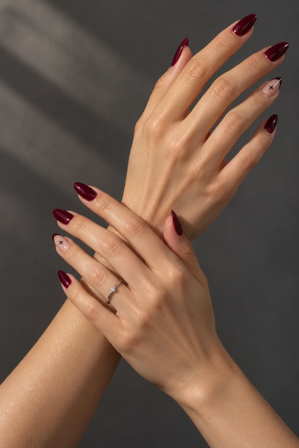 Matching glossy burgundy almond manicures with sheer star accents, shown on two hands crossing gently at the wrists.